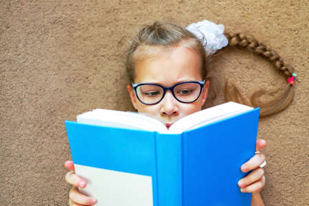 a girl on the floor reads a book when she is tired of sitting at a desk or table.の写真素材