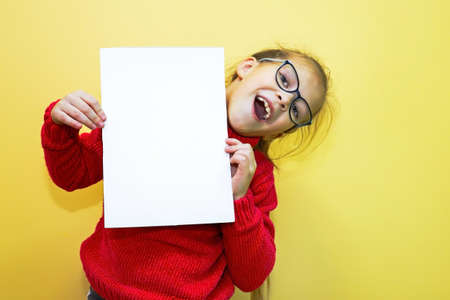 Child girl in a red sweater shows the mockup and makes a gesture with her hands and expresses...