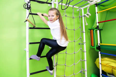 The girl smiles, plays and goes in for sports on the stairs and the Swedish wall in the children's...