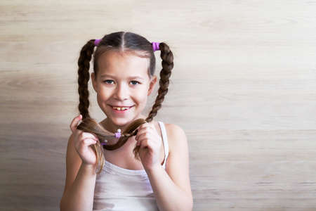 girl child with pigtails posing and showing off the length of her beautiful hair on a uniform background of a wooden wallの写真素材