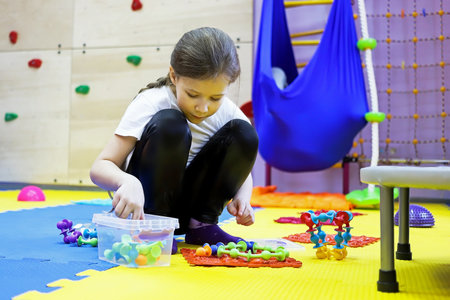 a child a girl on the floor of a children's rehabilitation center for correction collects a chain of viruses from a toy. the concept of lifestyleの写真素材