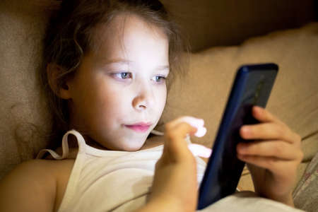 girl child hides from parents and secretly spoils his eyesight watching a fairy tale on the phone.