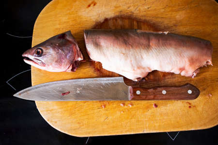 cut into pieces frozen salmon or salmon fish lies on a wooden board with a knife.の写真素材