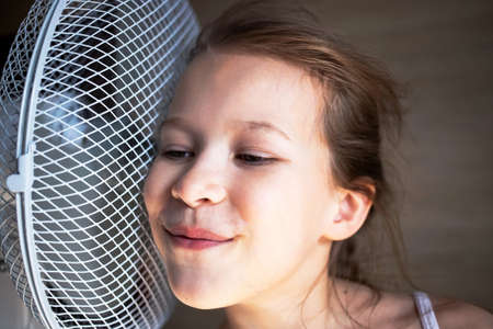 a little girl listens to the sound of wind and air from a large fan in the heat, very close is dangerous.の写真素材