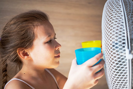 a little girl cools hot or warm water in the heat from the wind of a large fan in protest of the flag of ukraine.の写真素材