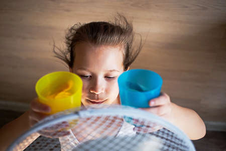 a little girl cools hot or warm water in the heat from the wind of a large fanの写真素材