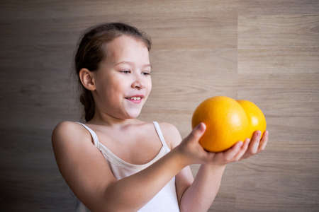 a little girl in a white t-shirt looks and shows orange citrus grapefruits estimates their weight as with dumbbells.の写真素材