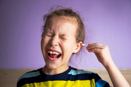 girl child in a striped turtleneck shows pain due to a cotton stick in the ear, where it is very...