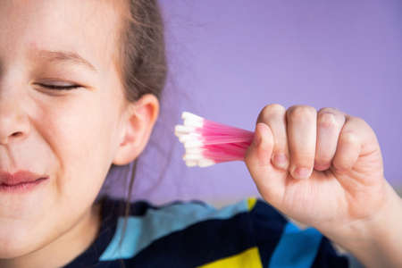 a child girl in a striped turtleneck puts a lot of cotton sticks in her ear, not much dirt will fitの写真素材