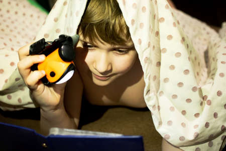 A teenager hides under a blanket and, in secret from his parents, spoils his eyesight and reads an interesting fairy tale with a flashlight.の写真素材