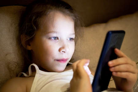 girl child hides from parents and secretly spoils his eyesight watching a fairy tale on the phone.の写真素材