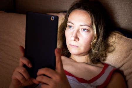 a young woman hides in bed at night and secretly spoils her eyesight watching movies on her phone.の写真素材