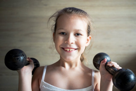 little girl child goes in for sports and poses with two black dumbbells, very hard.の写真素材