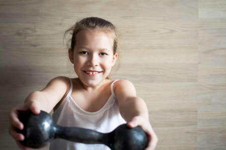 little girl child goes in for sports and poses with two black dumbbells, very hard.の写真素材