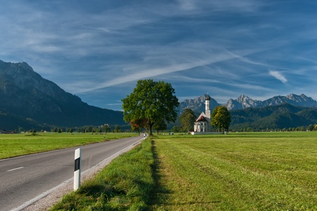 Autumn landscape with road, tree, church, mountains and sky on backgroundの写真素材