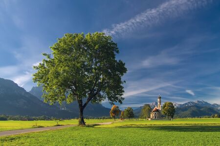 Autumn landscape with road, tree, church, mountains and sky on backgruondの写真素材