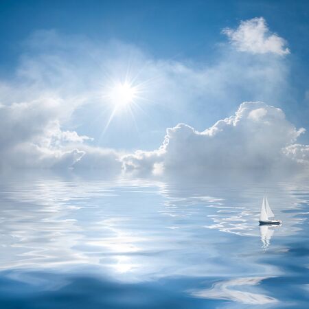 Blue sky with clouds and sun reflection in water; small yacht floats on the quiet seaの写真素材