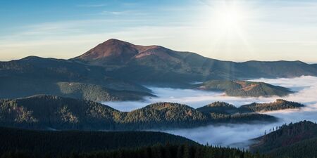 Mountain view with clouds below and rising sunの写真素材
