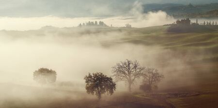 Autumn landscape with trees and fog, farmland view, Tuscanyの写真素材