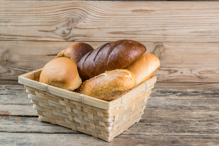 Assorted breads and wheat ears on old wooden board, food background