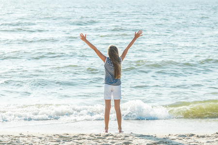 Happy teenage girl with hands up at sea beachの写真素材