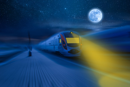 High-speed train passing station with motion blur, moon and stars in night skyの写真素材