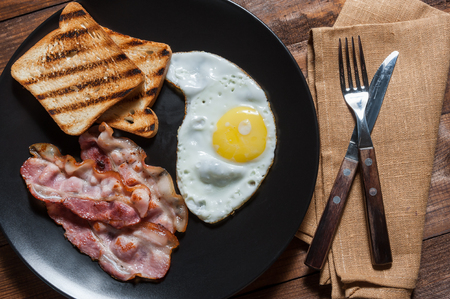Fried egg and bacon on plate, wooden rustic table, flat layの写真素材