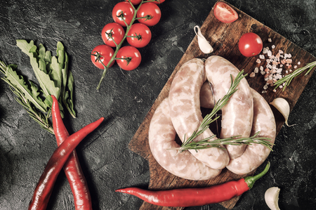 Raw sausages on cutting board, chili and tomatoes, kitchen rustic background, flat lay, vintage styleの写真素材