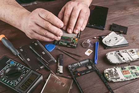 Broken cell phone repair. Smartphone parts and tools for recovery, selective focus. Film filter, vintage stylizationの写真素材
