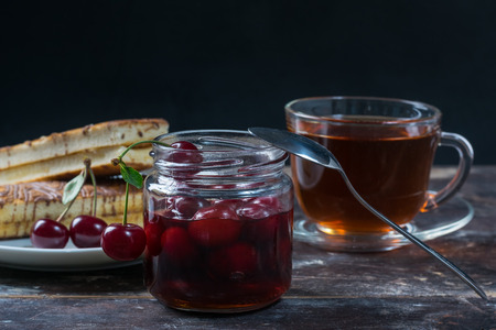 Cherry jam and tea on a wooden table. Sweet ripe berries in bowl. Delicious breakfast. Selective...