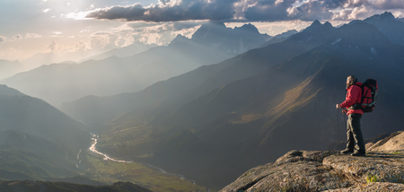Mountaineer with backpack on rock enjoying view of big mountains, hiking lifestyle, man on top.の写真素材
