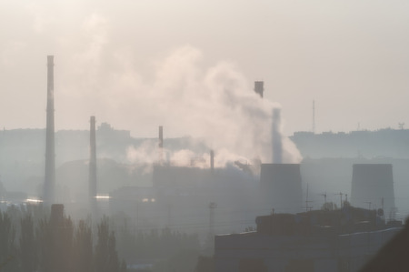 Industrial landscape with smoke from pipes, factory in city near residential buildings