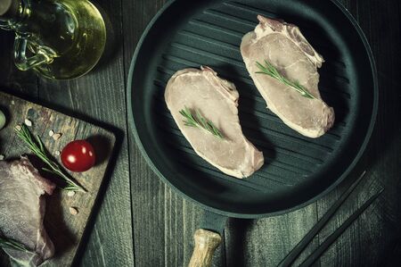 Pieces of raw pork on pan, ready to roast. Spices and oil, kitchen background. Retro stylization, vintage film filterの写真素材