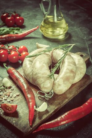 Raw sausages on cutting board, chili and tomatoes, kitchen rustic background, selective focus. Retro stylization, vintage film filterの写真素材