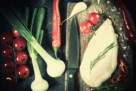Raw chicken fillet on cutting board, chili and tomatoes. Kitchen rustic background, Flat lay. Retro stylization, vintage film filterの写真素材