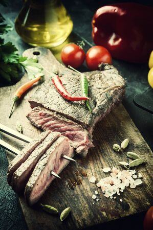 Grilled beef steak on wooden board. Hot meet with vegetables and spices. Retro stylization, vintage film filterの写真素材