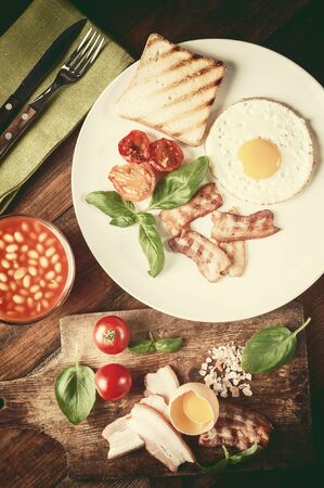 Fried eggs with bacon on breakfast on wooden rustic boards, food background. Retro stylization, vintage film filterの写真素材