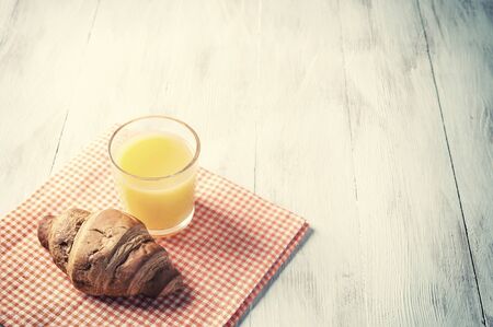 Breakfast with orange juise and croissant on wooden rustic table, food background. Retro stylization, vintage film filterの写真素材