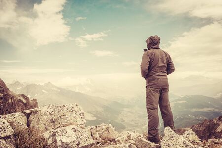 Hiker on mountain peak. Extremal sports and active life. Man at rock. Valley and sky on summer landscape. Vintage stylization, retro film filterの写真素材