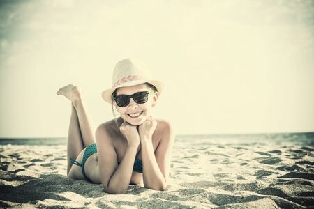 Cute white girl teenager resting on beach, summer view, selective focus. Vintage stylization, retro film filterの写真素材