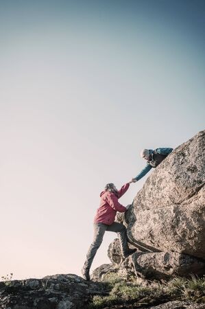 Two mans help each other hiking in mountains, friendship and teamwork support. Vintage stylization, retro film filterの写真素材