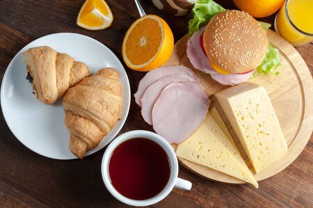 Croissants and sausages with tea on breakfast. Orange juise and sandwich on wooden rustic boards, food background. Flat layの写真素材