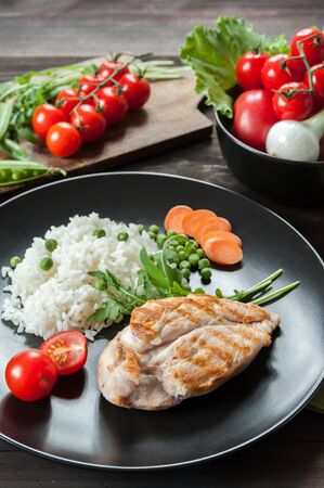 Grilled chicken fillet on plate with boiled rice. Raw vegetables, kitchen background. Selective focusの写真素材