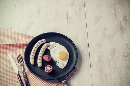 Fried eggs with sausage on pan. Breakfast on wooden rustic table, food background. Retro stylization, vintage film filterの写真素材