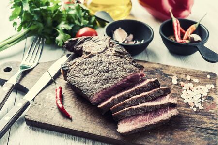 Fried beef steak on wooden board. Hot meet with vegetables and spices. Selective focus. Retro stylization, vintage film filterの写真素材