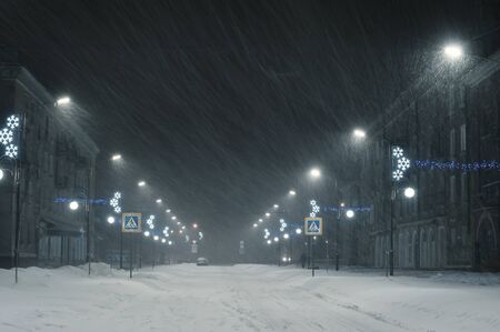 Night winter landscape with snowstorm in city. Snowy streets and bright lanterns. Vintage stylization, retro film filterの写真素材