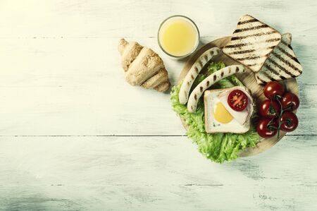 Fried eggs with sausages and vegetables. Breakfast with orange juise and croissant on wooden rustic boards, food background. Vintage stylization, retro film filterの写真素材