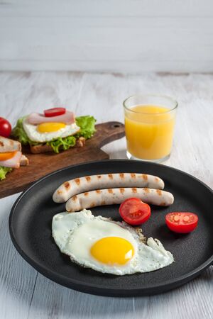 Fried sausage with eggs and vegetables on pan. Delicious breakfast with orange juise and croissant on wooden rustic boards, food background.の写真素材