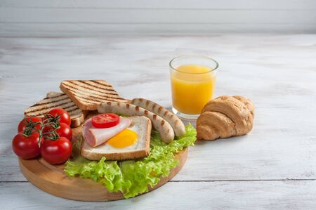 Fried sausage with eggs and vegetables. Delicious breakfast with orange juise and croissant on wooden rustic boards, food background.の写真素材