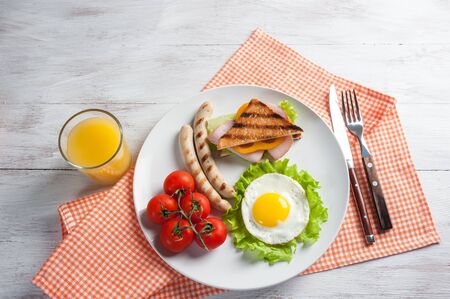 Fried sausage with eggs and vegetables on plate. Delicious breakfast with orange juise and croissant on wooden rustic boards, food background.の写真素材